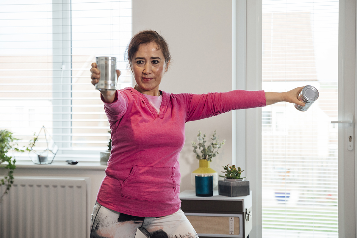 Senior woman standing in the living room of her home doing weight training with cans.