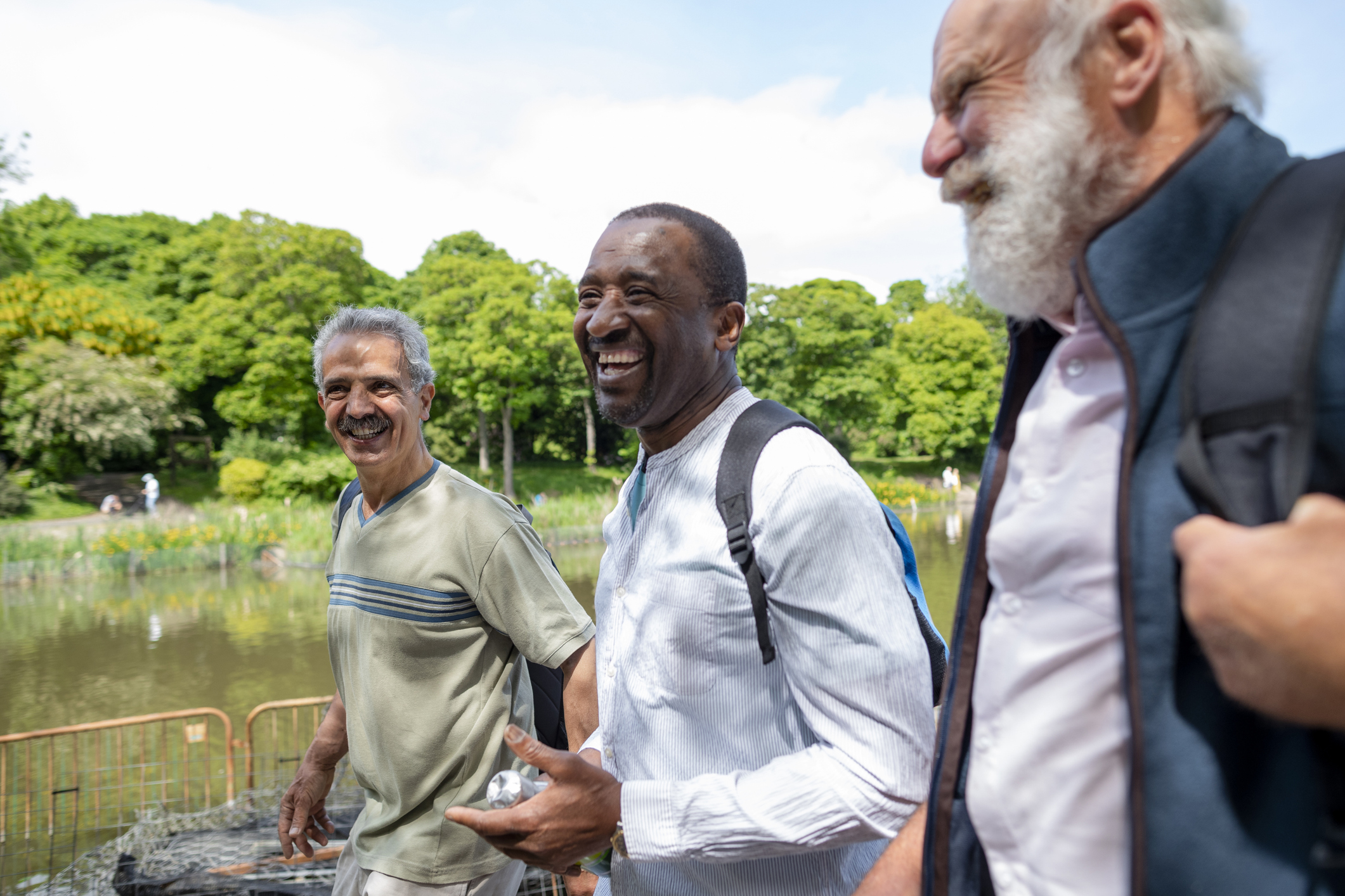 baker-12 Three senior men exploring leazes park and enjoying a day out together in Newcastle Upon Tyne, England. They are walking next to a lake while they walk, talk and laugh with each other.