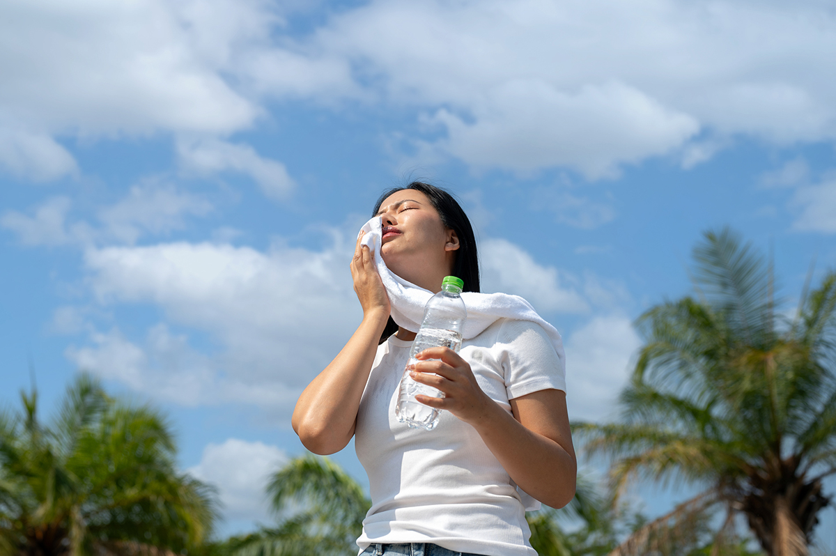 A beautiful women in white t shirt holding a water bottle and wiping her sweat in the sunlight after running in the park. outdoor exercise, hot weather.